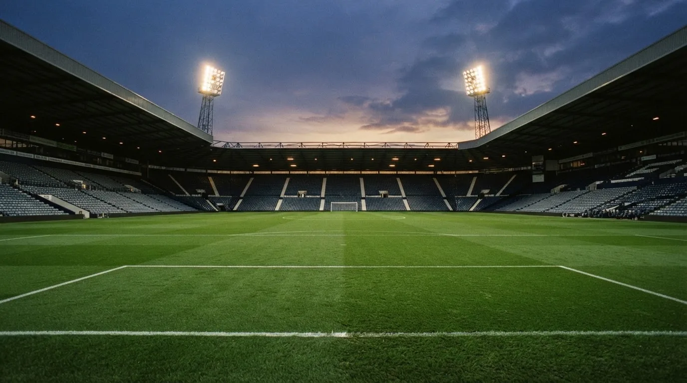 An empty football stadium with floodlight masts at dusk