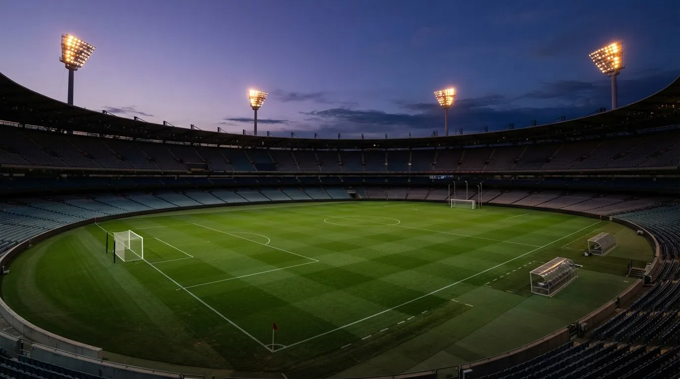 An empty football stadium with floodlight masts at dusk