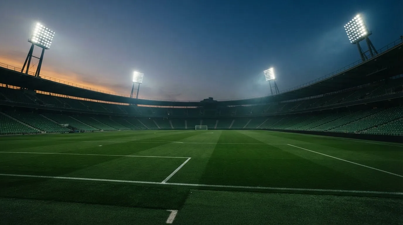 An empty football stadium with floodlight masts at dusk