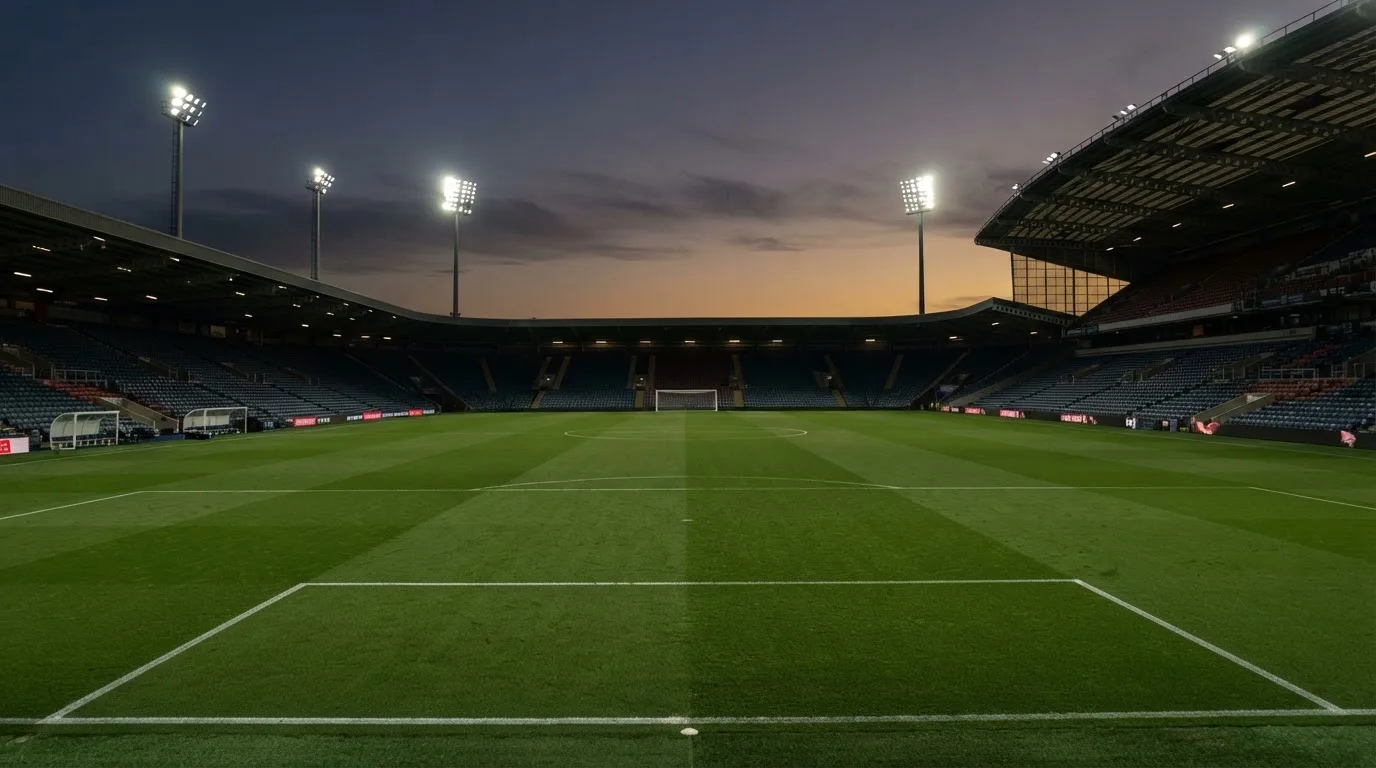 An empty football stadium with floodlight masts at dusk